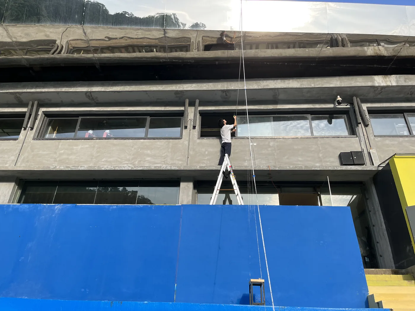 The artist on a ladder fixing the light line to the concrete facade of the stand