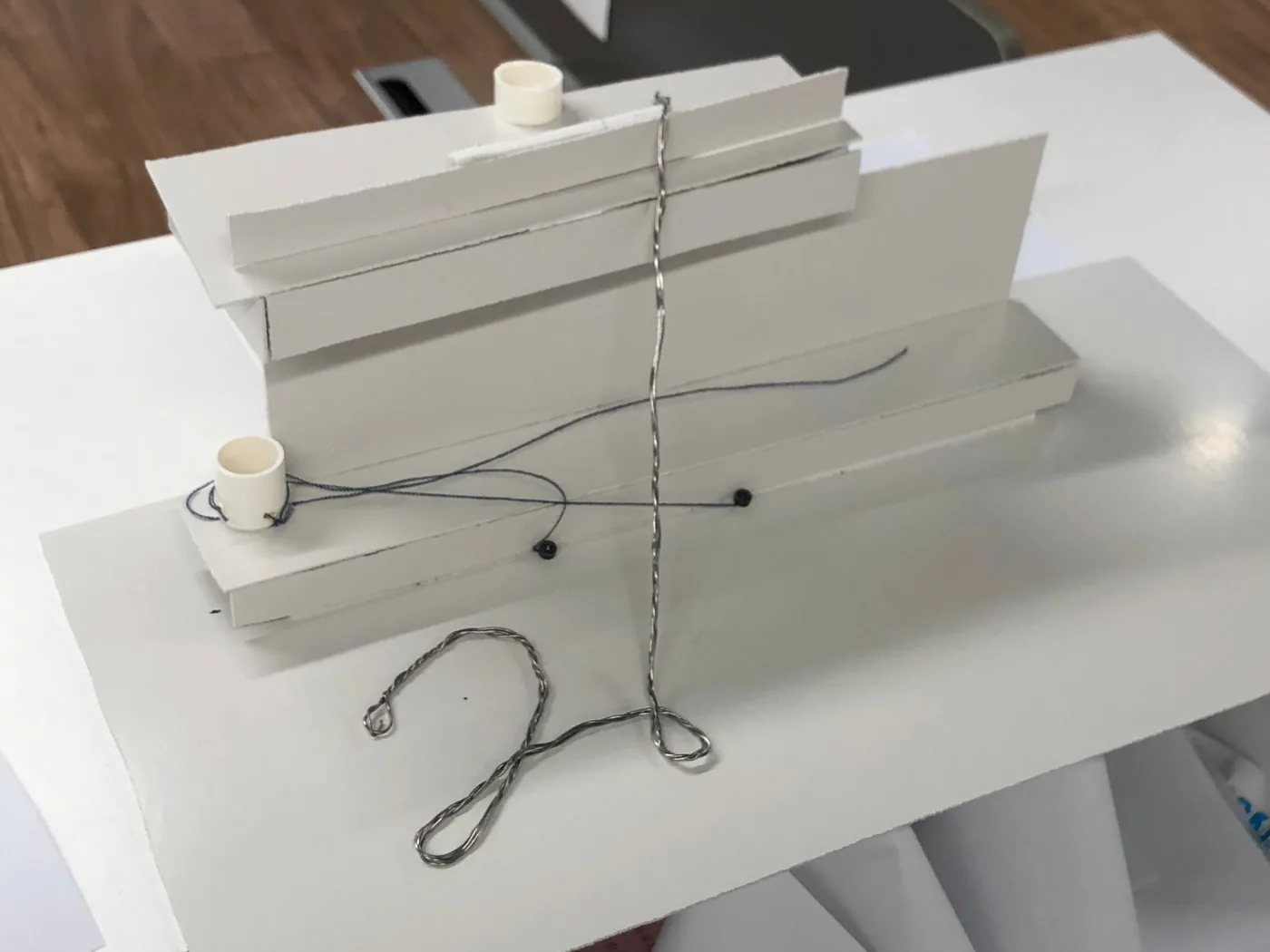 White card model of the stand with a twisted wire line running from a figure on the ground to the roof