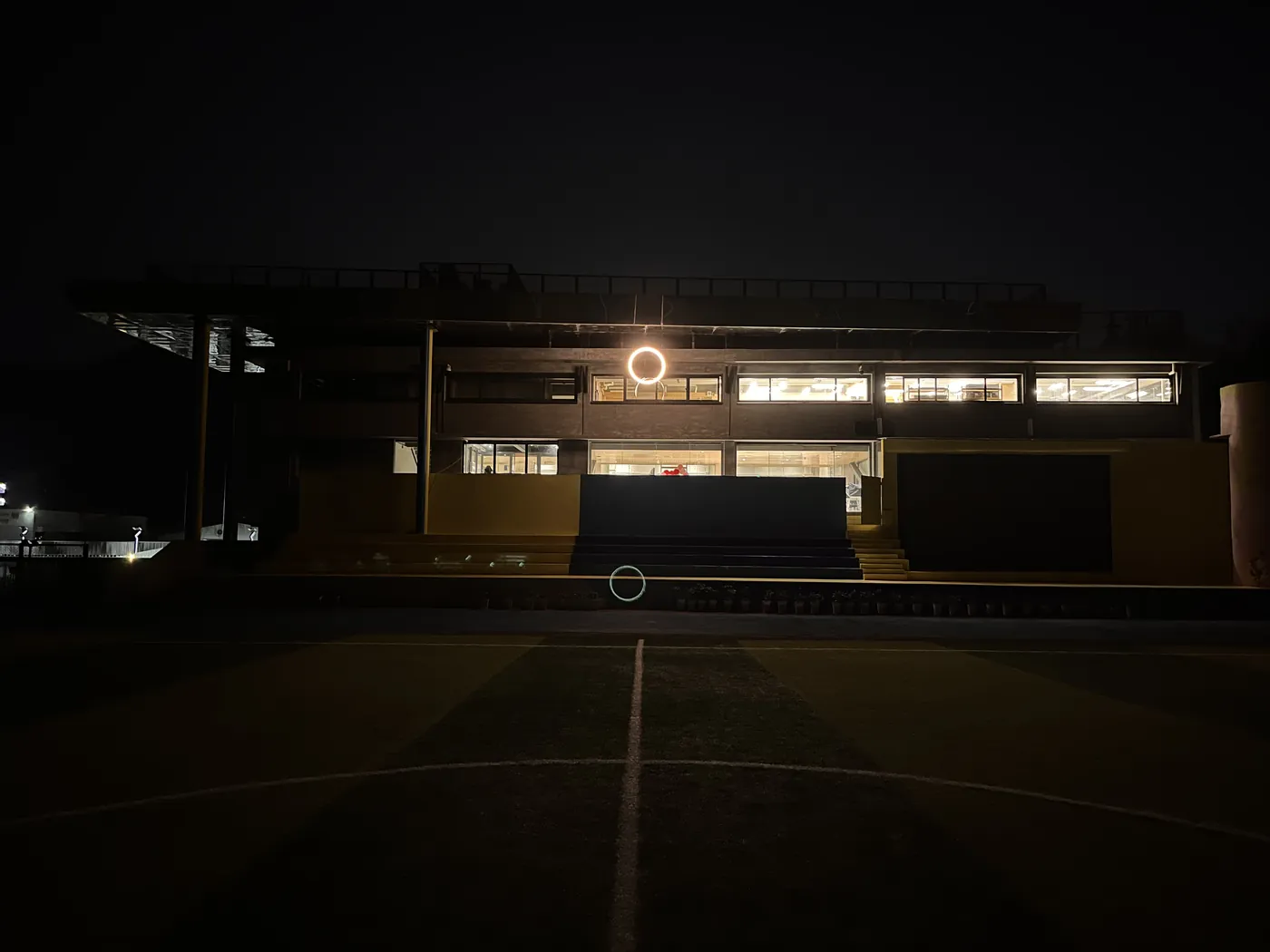 A small ring of light on the facade of the school building at night, seen across the sports ground
